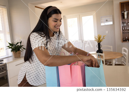 Smiling woman unpacking colorful shopping bags at home in kitchen 135634392