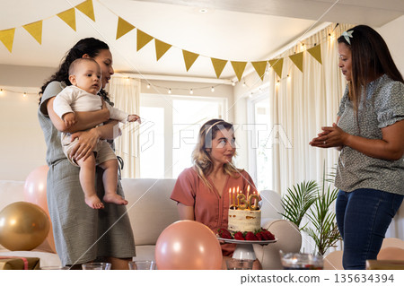 Celebrating birthday, woman holding cake with candles while friends gather around 135634394