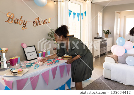 Woman decorating table with cupcakes and gifts at home baby shower celebration Woman decorating table with cupcakes and gifts at home baby shower celebration 135634412