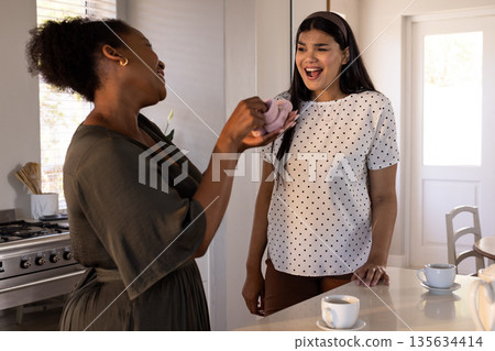 African American woman giving gift to surprised friend in kitchen, both smiling African American woman giving gift to surprised friend in kitchen, both smiling 135634414