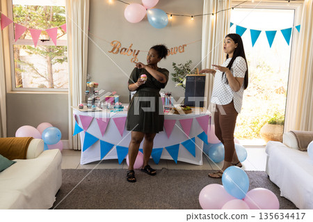 Celebrating baby shower, two women enjoying cupcakes and decorations in living room Celebrating baby shower, two women enjoying cupcakes and decorations in living room 135634417