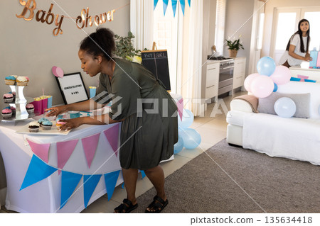 Woman arranging cupcakes at baby shower while friend decorates with balloons Woman arranging cupcakes at baby shower while friend decorates with balloons 135634418