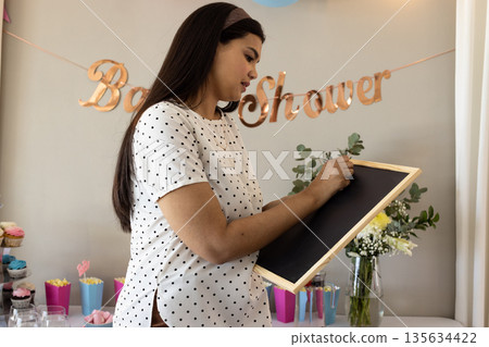 Woman writing on chalkboard at baby shower, surrounded by decorations and flowers 135634422