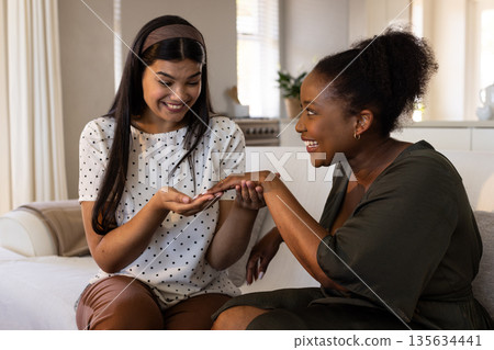 Two women joyfully sharing moment at home, admiring ring together Two women joyfully sharing moment at home, admiring ring together 135634441