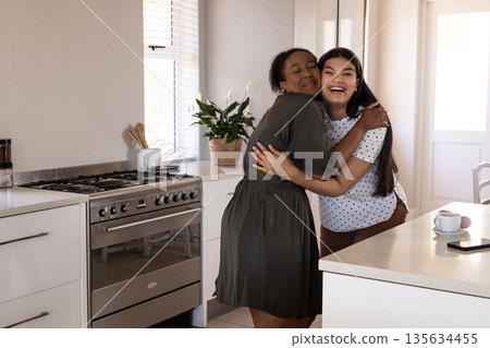 In kitchen, African American woman hugging friend, celebrating joyful moment together In kitchen, African American woman hugging friend, celebrating joyful moment together 135634455