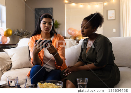 Friends watching video on smartphone while sitting on couch during celebration Friends watching video on smartphone while sitting on couch during celebration 135634468