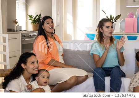 Women and baby sitting on couch, joyfully watching something exciting at home 135634472