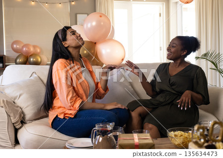 Women laughing and enjoying conversation on sofa during festive home gathering Women laughing and enjoying conversation on sofa during festive home gathering 135634473