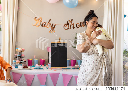 Smiling woman holding baby at baby shower celebration with decorations and cupcakes Smiling woman holding baby at baby shower celebration with decorations and cupcakes 135634474