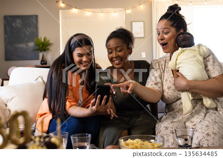 Friends enjoying time together at home, smiling and looking at smartphone Friends enjoying time together at home, smiling and looking at smartphone 135634485