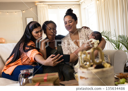 Friends taking selfie on couch, celebrating birthday with cake and gifts nearby Friends taking selfie on couch, celebrating birthday with cake and gifts nearby 135634486