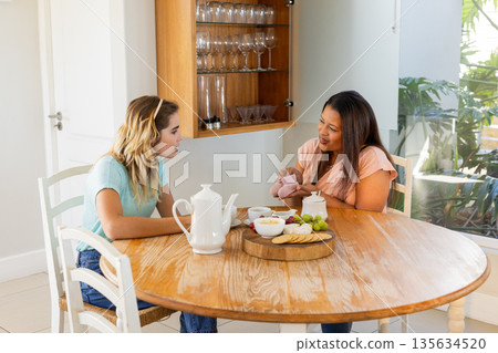 Two women enjoying tea and snacks at home, engaged in friendly conversation 135634520