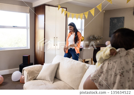 Smiling woman in orange shirt enjoying family celebration at home with balloons 135634522