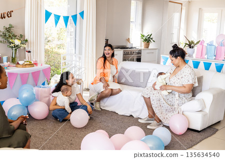 Women enjoying baby shower celebration with balloons and gifts in living room Women enjoying baby shower celebration with balloons and gifts in living room 135634540