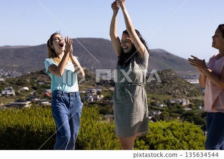 Women celebrating outdoors, raising hands and clapping with joyful expressions Women celebrating outdoors, raising hands and clapping with joyful expressions 135634544