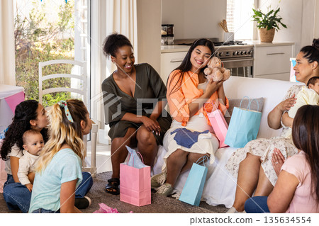 Women celebrating baby shower at home, exchanging gifts and smiling joyfully Women celebrating baby shower at home, exchanging gifts and smiling joyfully 135634554