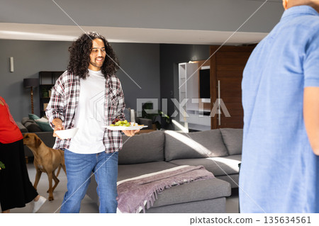 Man carrying plates with snacks at home during celebration, smiling happily 135634561