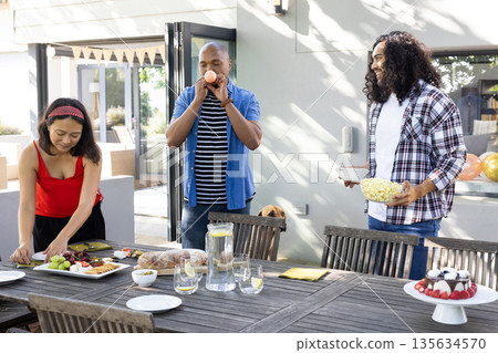 Friends preparing outdoor table with snacks and drinks, enjoying festive gathering Friends preparing outdoor table with snacks and drinks, enjoying festive gathering 135634570