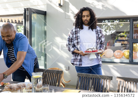 Carrying cake and arranging decorations, friends setting outdoor table for celebration 135634572