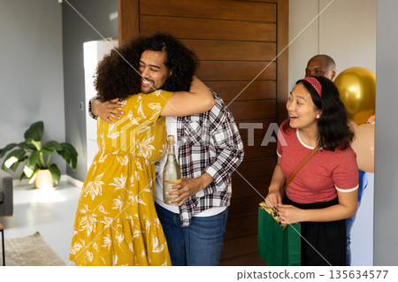 Friends celebrating at home, hugging and exchanging gifts with joyful smiles Friends celebrating at home, hugging and exchanging gifts with joyful smiles 135634577