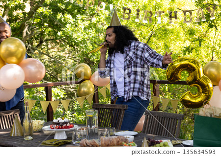 Man celebrating birthday outdoors, blowing party horn with joyful expression Man celebrating birthday outdoors, blowing party horn with joyful expression 135634593