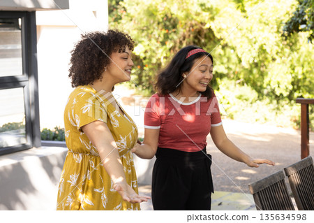 Friends laughing and enjoying outdoor conversation on sunny day in garden 135634598