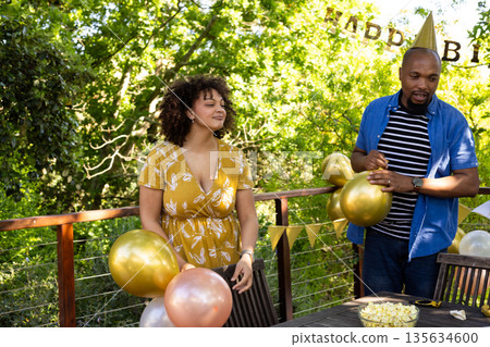 Friends decorating with balloons, celebrating birthday outdoors on sunny day 135634600