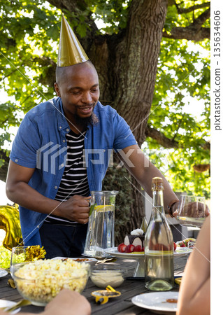 African American man wearing party hat serving drinks at outdoor celebration African American man wearing party hat serving drinks at outdoor celebration 135634606