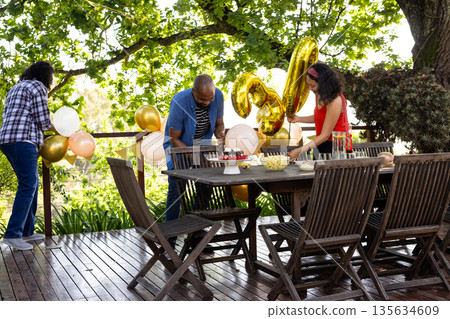 Friends decorating outdoor patio with balloons and snacks for birthday celebration Friends decorating outdoor patio with balloons and snacks for birthday celebration 135634609