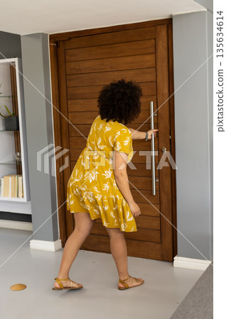 African American woman in yellow dress opening door, preparing to welcome guests African American woman in yellow dress opening door, preparing to welcome guests 135634614