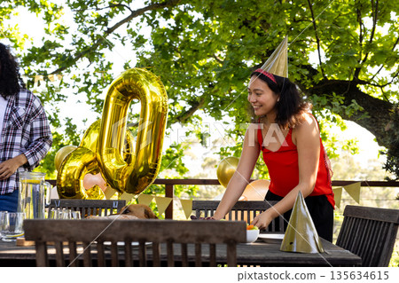 Setting table outdoors, woman in red dress arranging for birthday with balloons Setting table outdoors, woman in red dress arranging for birthday with balloons 135634615