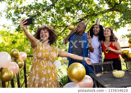 Friends celebrating outdoors, taking selfie with party hats and balloons Friends celebrating outdoors, taking selfie with party hats and balloons 135634628
