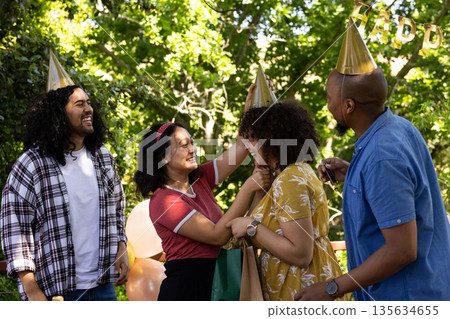 Celebrating outdoors, friends wearing party hats, laughing in festive atmosphere 135634655