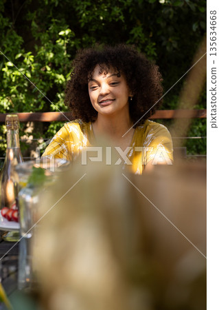 Smiling woman enjoying outdoor gathering with friends, sunlight on her face 135634668