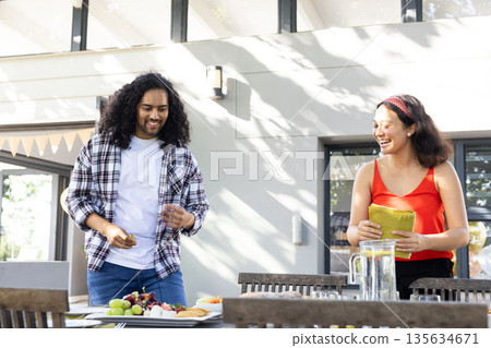 Friends preparing outdoor table with food and drinks, smiling and enjoying together Friends preparing outdoor table with food and drinks, smiling and enjoying together 135634671