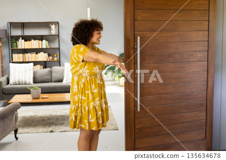 African American woman in yellow dress welcoming someone at home with open arms African American woman in yellow dress welcoming someone at home with open arms 135634678