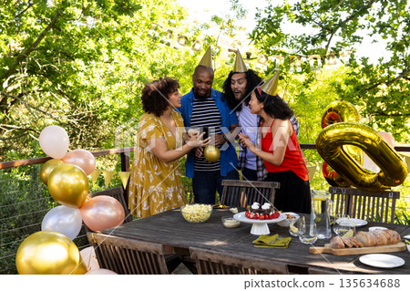 Friends celebrating birthday outdoors, wearing party hats and sharing joyful moments Friends celebrating birthday outdoors, wearing party hats and sharing joyful moments 135634688