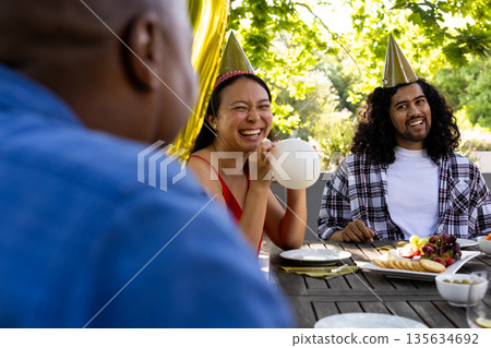 Celebrating outdoors, friends wearing party hats, laughing at festive gathering Celebrating outdoors, friends wearing party hats, laughing at festive gathering 135634692