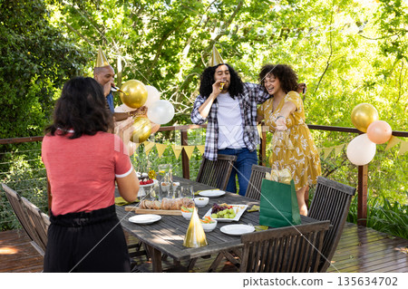 Celebrating birthday outdoors, friends wearing party hats in festive atmosphere Celebrating birthday outdoors, friends wearing party hats in festive atmosphere 135634702