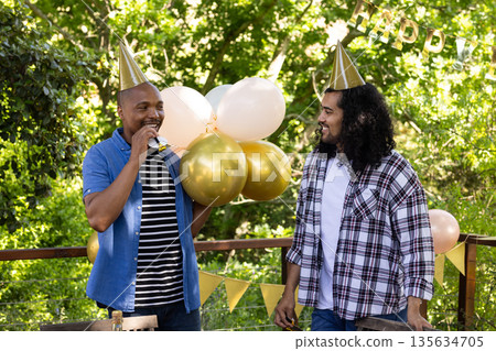 Friends celebrating outdoors wearing party hats and enjoying festive balloons 135634705