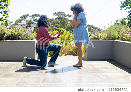 Man proposing to surprised woman outdoors, both expressing joy and excitement 135634721