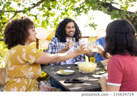 Friends toasting with drinks at outdoor gathering, enjoying celebration under trees Friends toasting with drinks at outdoor gathering, enjoying celebration under trees 135634724