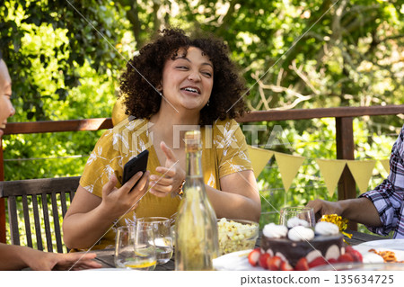 Laughing woman holding smartphone at outdoor party with friends and cake 135634725