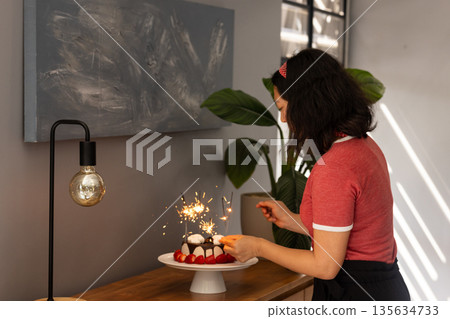 Woman decorating cake with sparklers at home, preparing for celebration 135634733