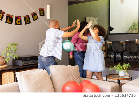 African American couple celebrating at home with high-fives and colorful balloons 135634736