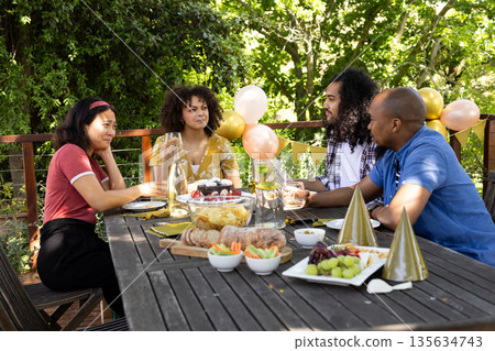Friends enjoying outdoor celebration with food and drinks on sunny day Friends enjoying outdoor celebration with food and drinks on sunny day 135634743
