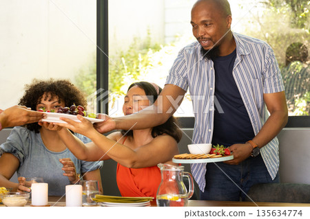 African American man serving food to friends at home, enjoying festive gathering 135634774