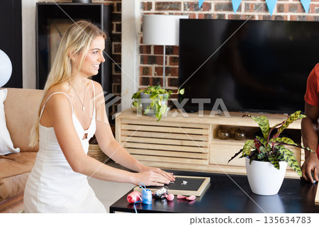 Smiling woman in white dress preparing gift at home for celebration Smiling woman in white dress preparing gift at home for celebration 135634783