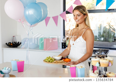 Smiling woman preparing snacks for party with balloons and decorations at home Smiling woman preparing snacks for party with balloons and decorations at home 135634784