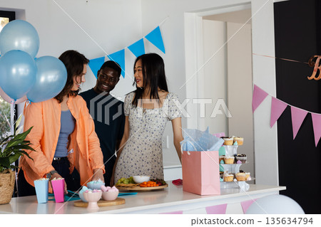 Celebrating at home, friends chatting happily with cupcakes and colorful decorations Celebrating at home, friends chatting happily with cupcakes and colorful decorations 135634794